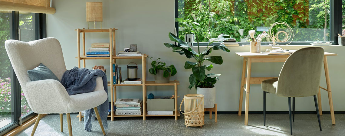 Grauer Sessel am Fenster und ein Raumteiler aus Bambus im Hintergrund. Laterne aus Bambus auf dem Boden neben einem Bambusschreibtisch und einem olivgrünen Esszimmerstuhl.