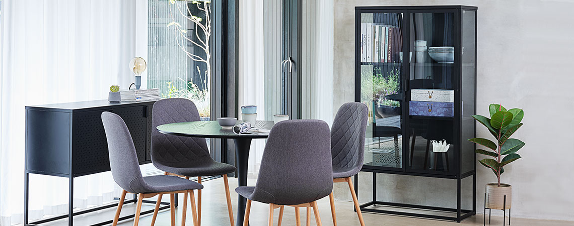 Glasvitrine in einem Esszimmer mit einem runden Esstisch und vier grauen Stühlen