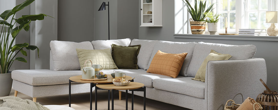 Wohnzimmereinrichtung mit einem grauen Sofa und orange-, grün- und beigefarbenen Zierkissen