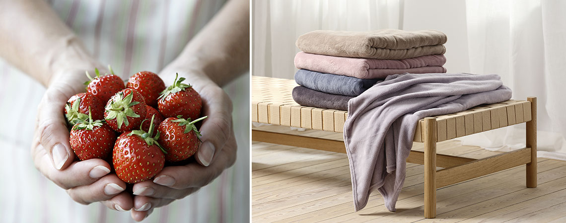 Eine Frau mit frischen Erdbeeren in der Hand und einem Tagesbett mit einem Stapel Decken in Sommerfarben 