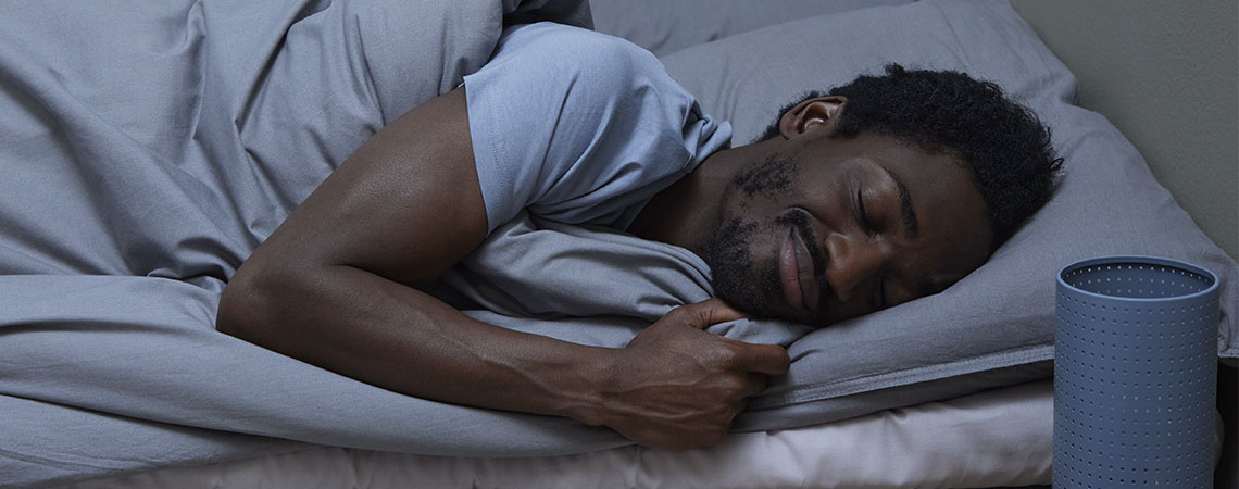 Mann schläft in einem Bett mit grauer Bettwäsche