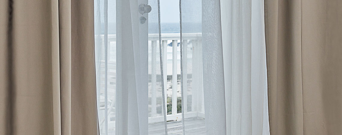 Blick auf einen Balkon durch eine geöffnete Tür mit flatternden Vorhängen
