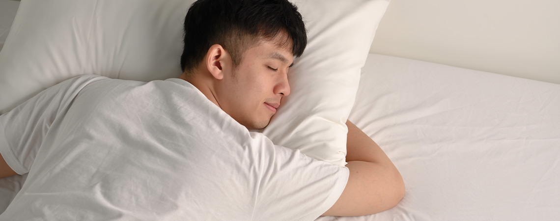 Mann schläft friedlich im Bett mit weißem Kissen und weißem Topper
