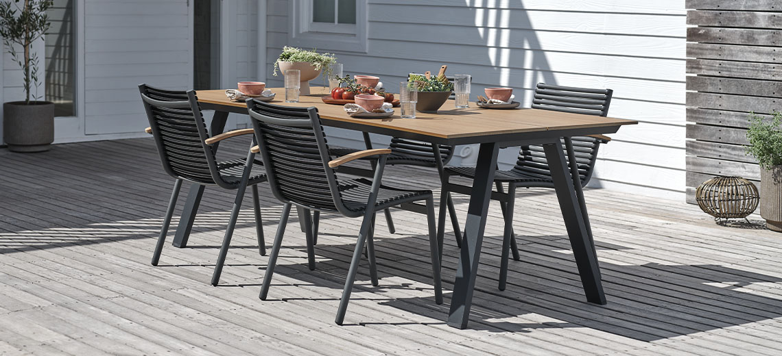 Gartentisch aus Holz mit schwarzen Beinen und vier Gartenstühlen auf der Terrasse