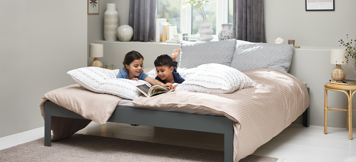 Zwei Kinder die auf einem Doppelbett mit Duvet und Bettdeckenbezug, Kopfkissen und Zierkissen ein Buch lesen