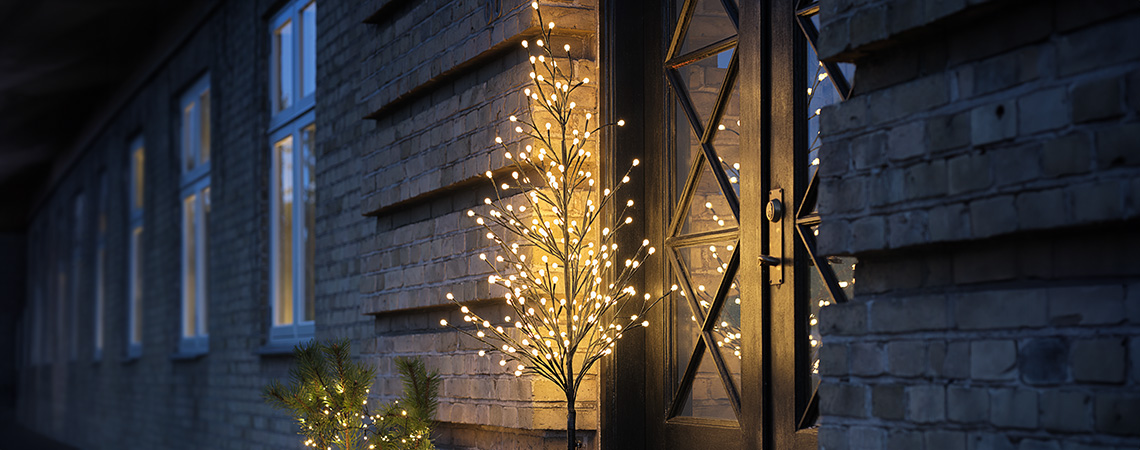 Außen-Weihnachtsbeleuchtung – LED-Lichterbaum neben der Haustür eines Hauses