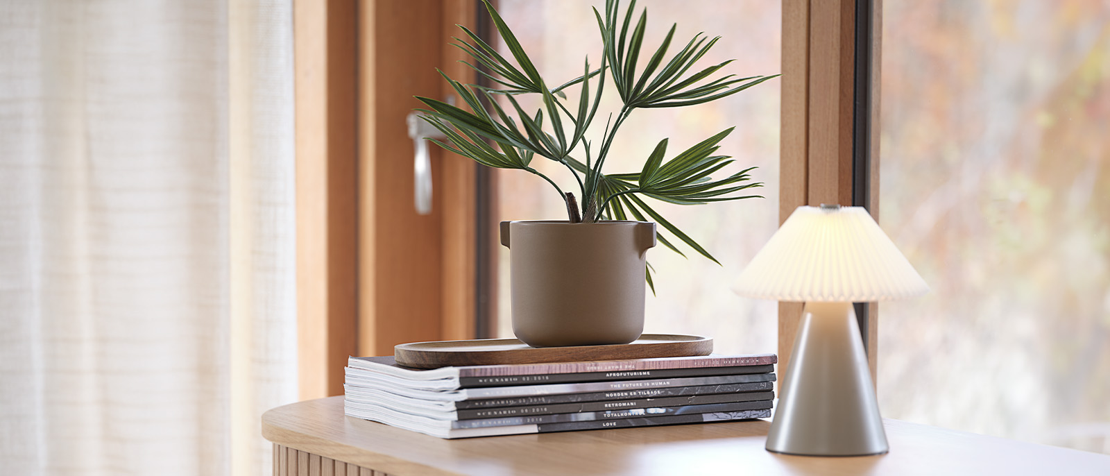 Kunstpflanze im Blumentopf auf einem Schreibtisch mit Büchern und einer Tischlampe