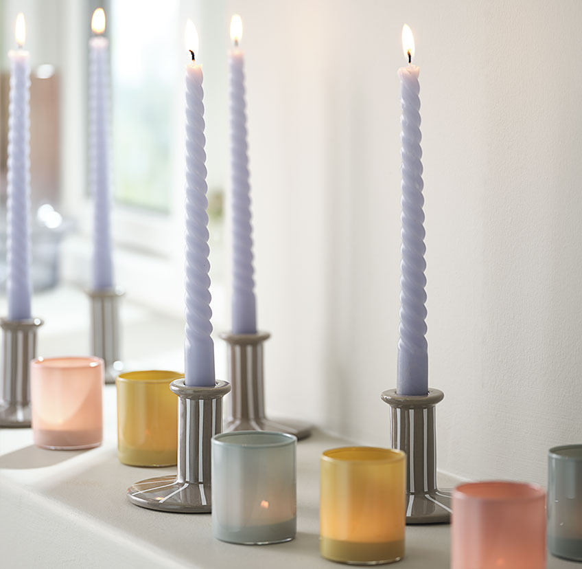 Hellblaue, gedrehte Kerzen in Kerzenhalter mit weißen Streifen und Teelichterhalter in blau, gelb und rot 
