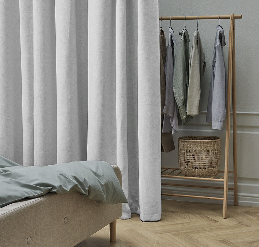 Beiger Vorhang vor einem Kleiderständer als Trennelement zwischen Schlaf- und Garderobenbereich