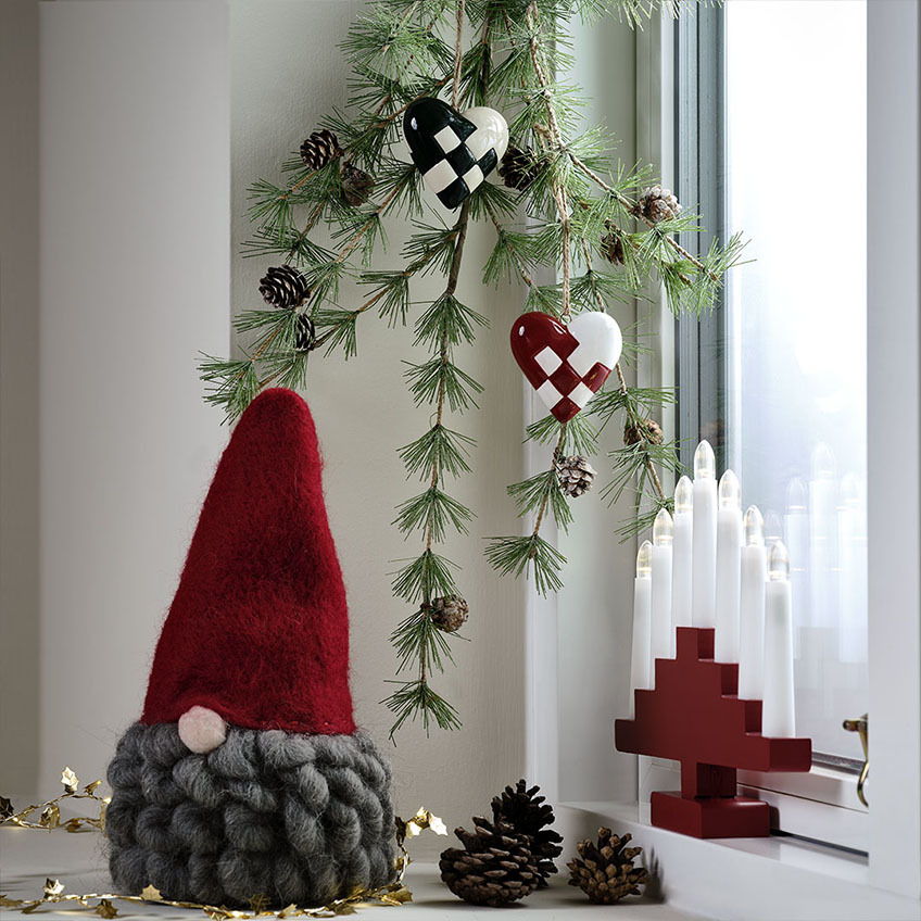 Weihnachtswichtel mit roter Mütze und grauem Bart, Weihnachtsherz-Deko und roter Kerzenbogen