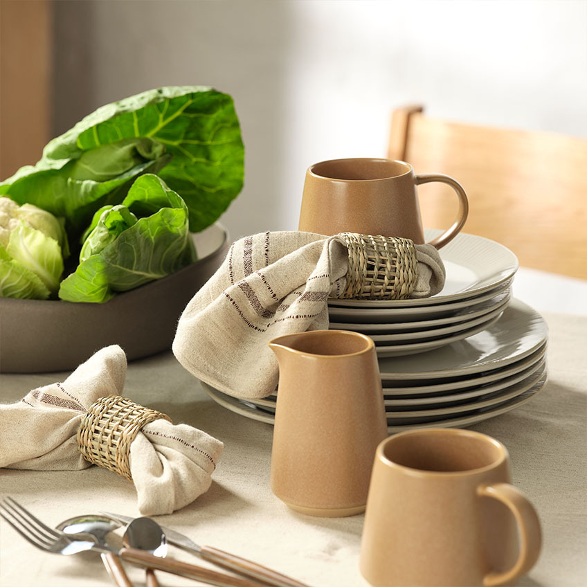 Geschirr und Tischgedeck: Becher, Milchkännchen, Stoffservietten mit Serviettenringen und Salatschüssel auf dem Esstisch