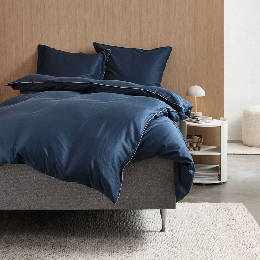 Satin-Bettwäsche in Dunkelblau mit hellblauer Biese auf einem Bett im Schlafzimmer