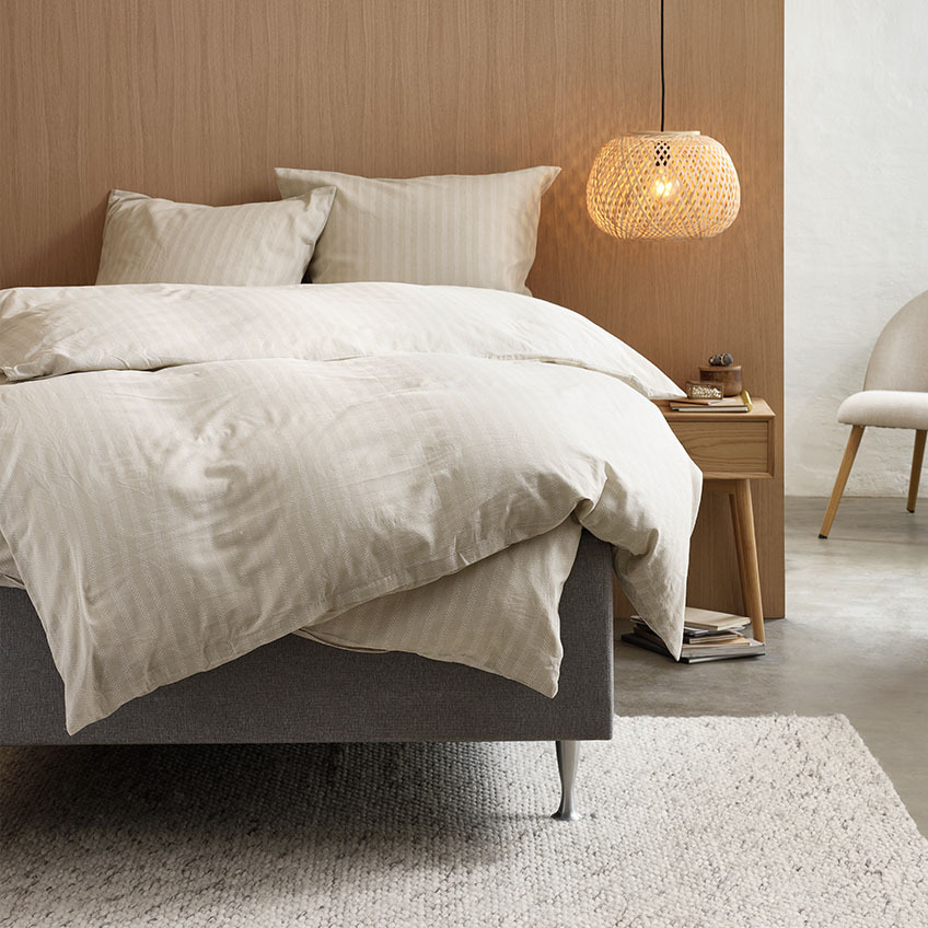Bettwäsche aus Baumwolle in warmen Beigetönen mit Streifenmuster auf einem Bett im Schlafzimmer