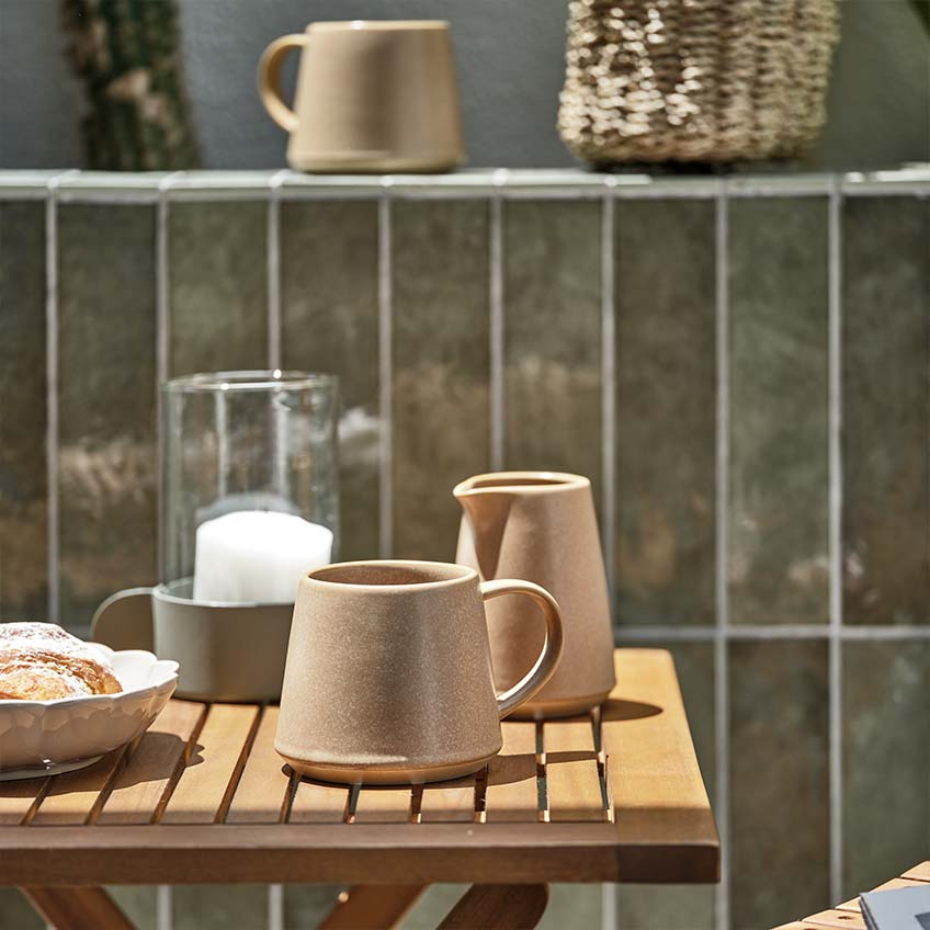 Kaffeetasse und Milchkanne auf einem kleinen Holztisch in der Sonne