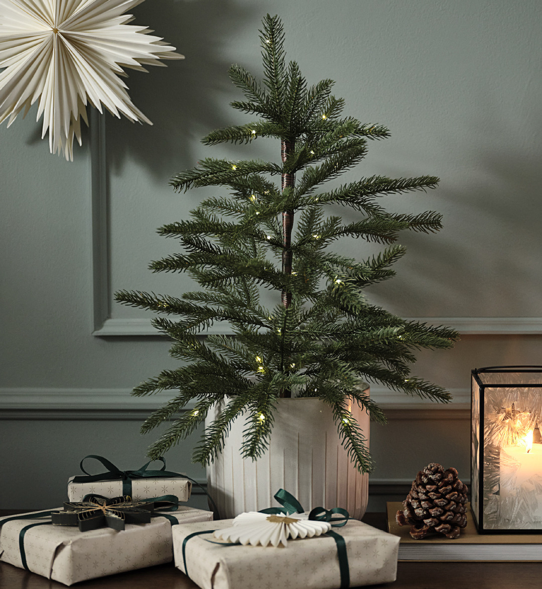 Künstlicher Weihnachtsbaum in einem Topf mit Lichtern und einem Papierstern an der Wand 