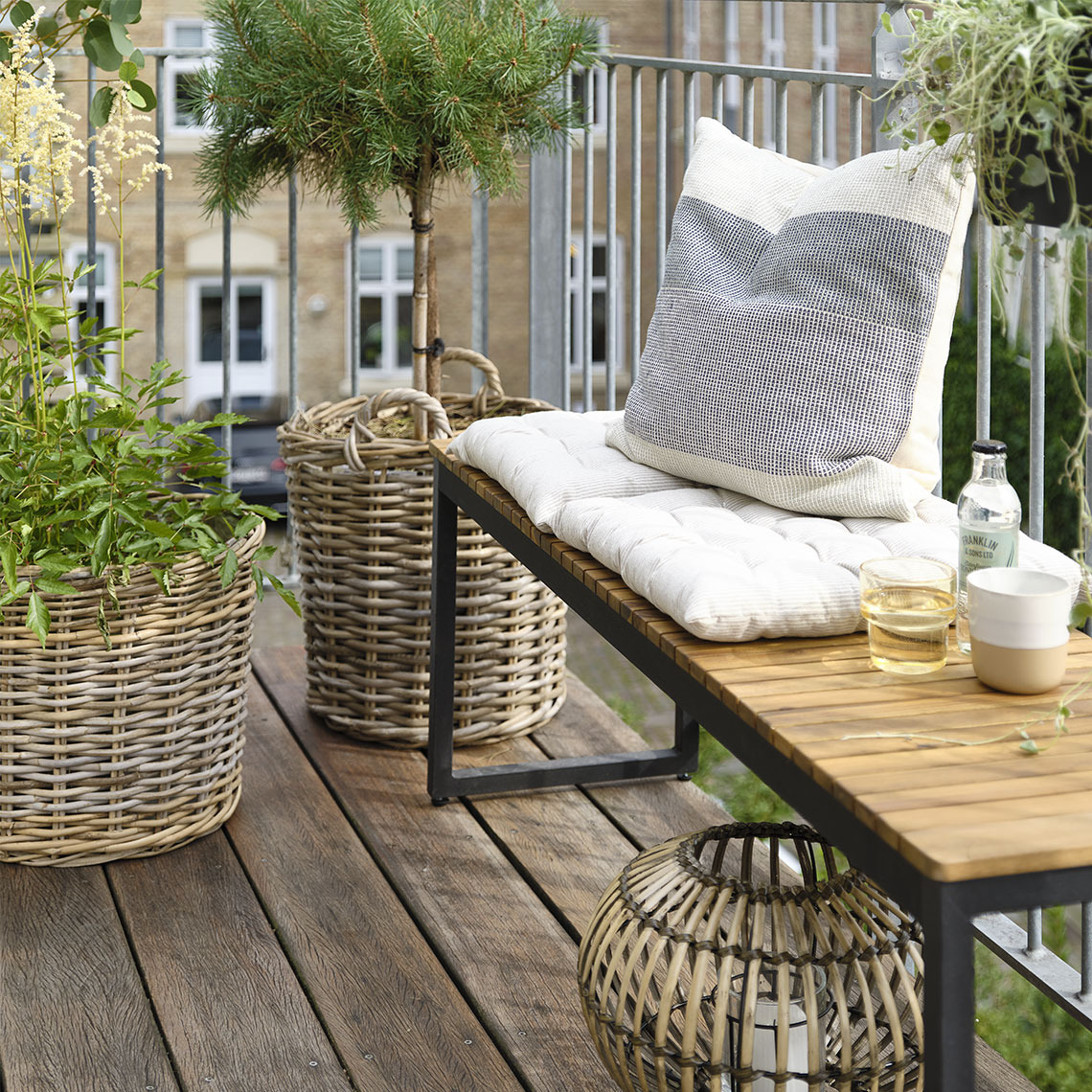 Gartenbank aus Baum und Metall auf einem kleinen Balkon mit Pflanzen und Pflanzgefäßen