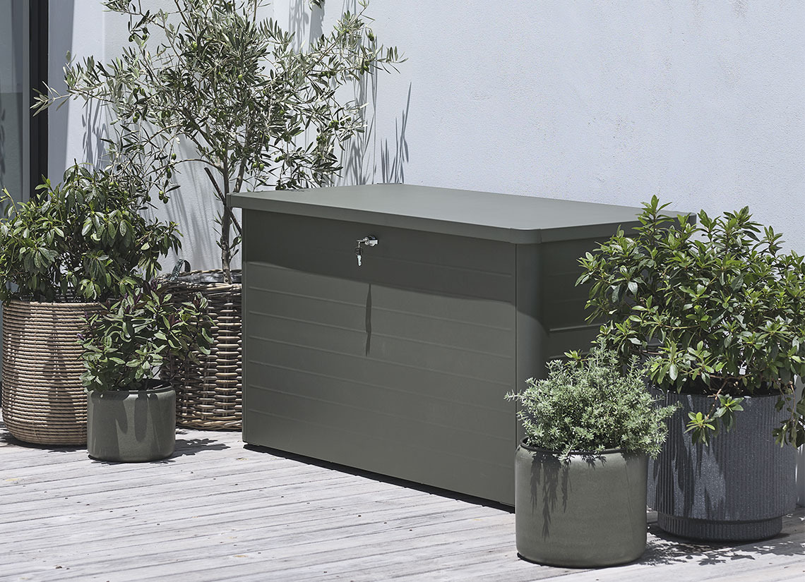 Graue Gartenkissenbox auf einer Terrasse mit Pflanzen und Pflanzgefäßen
