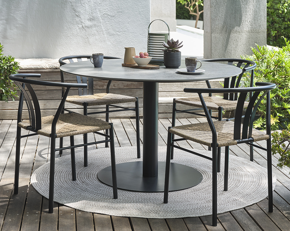 Grauer VAMDRUP-Gartentisch und TAGMARK-Gartenstühle Sockel-Gartentisch mit vier Gartenstühlen auf einer Veranda