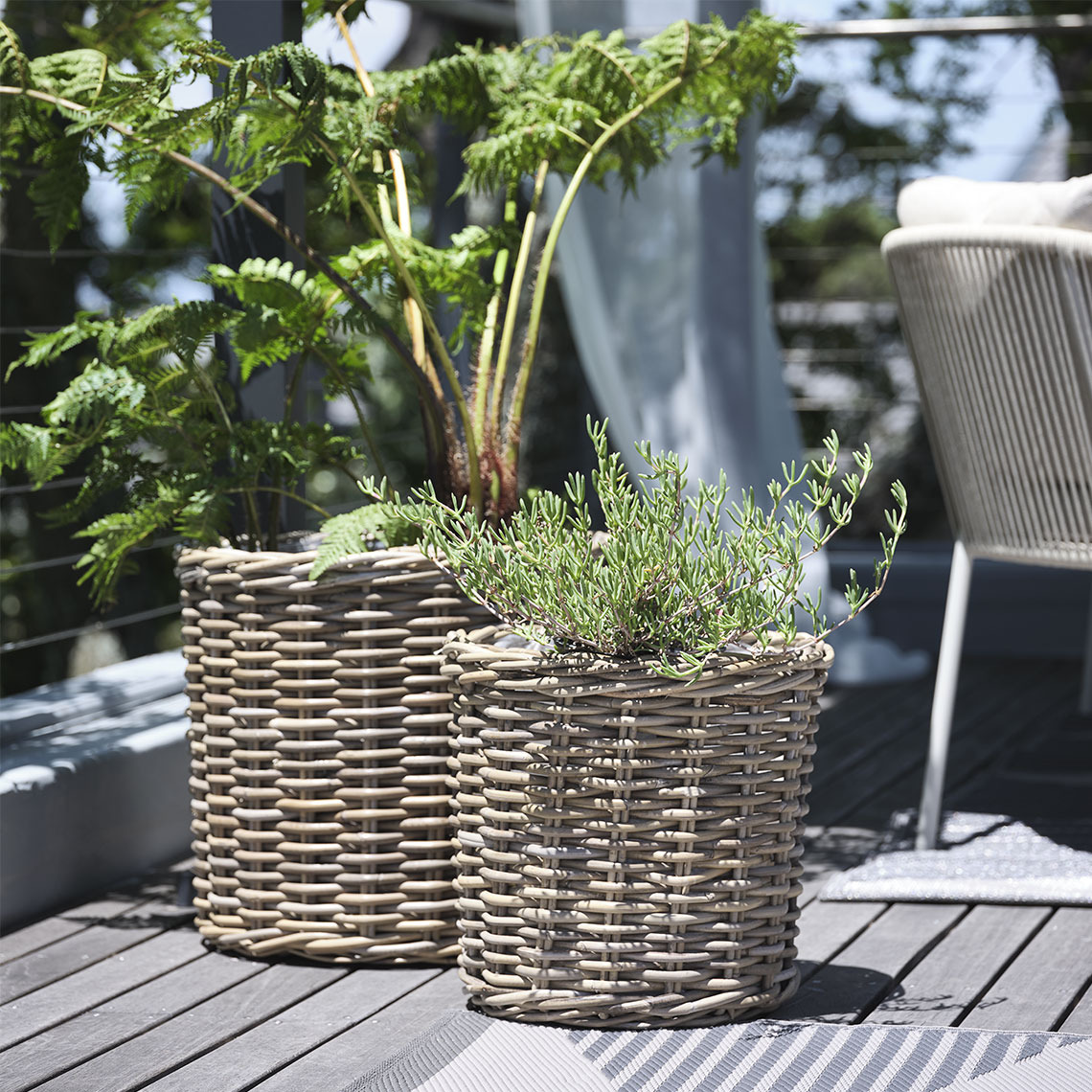 Two planter baskets in natural, untreated rattan standing on a balcony with plants