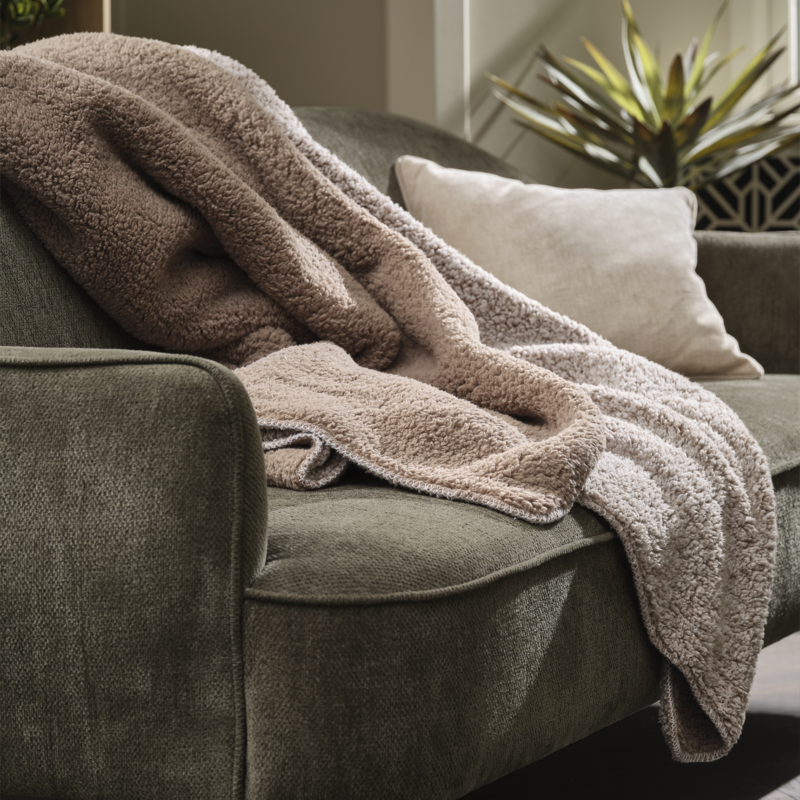 Kuscheldecke in beige auf einem grünen Sofa