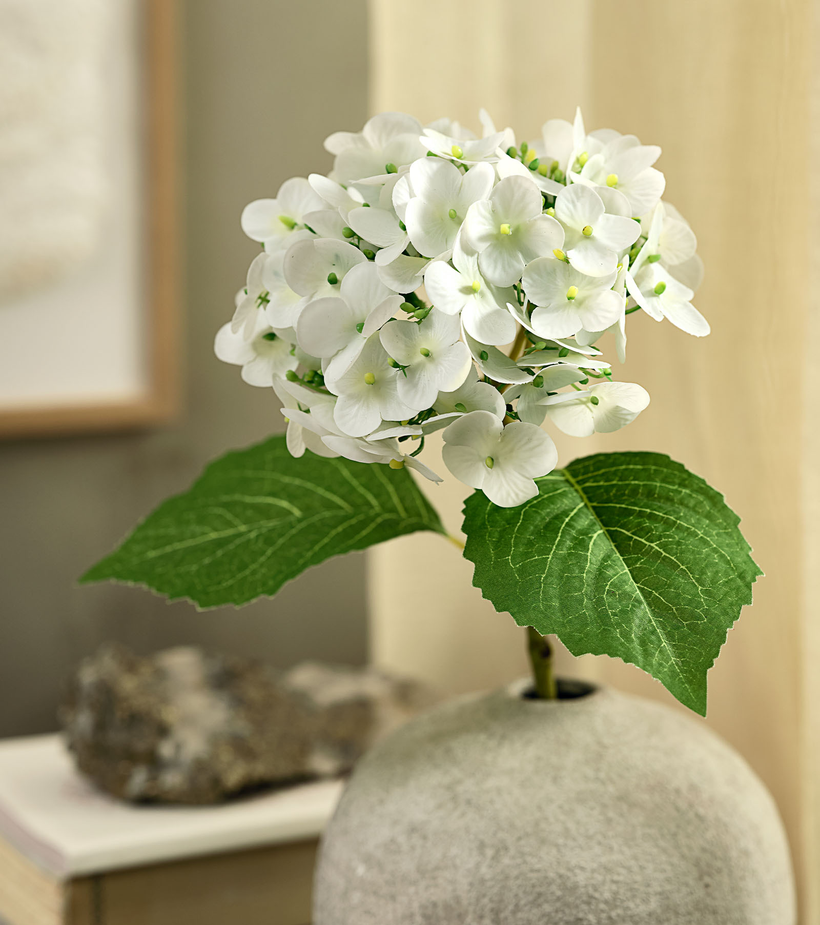 Künstliche Blume (Nachbildung einer weißen Hortensie) mit grünen Blättern in einer rustikalen Vase