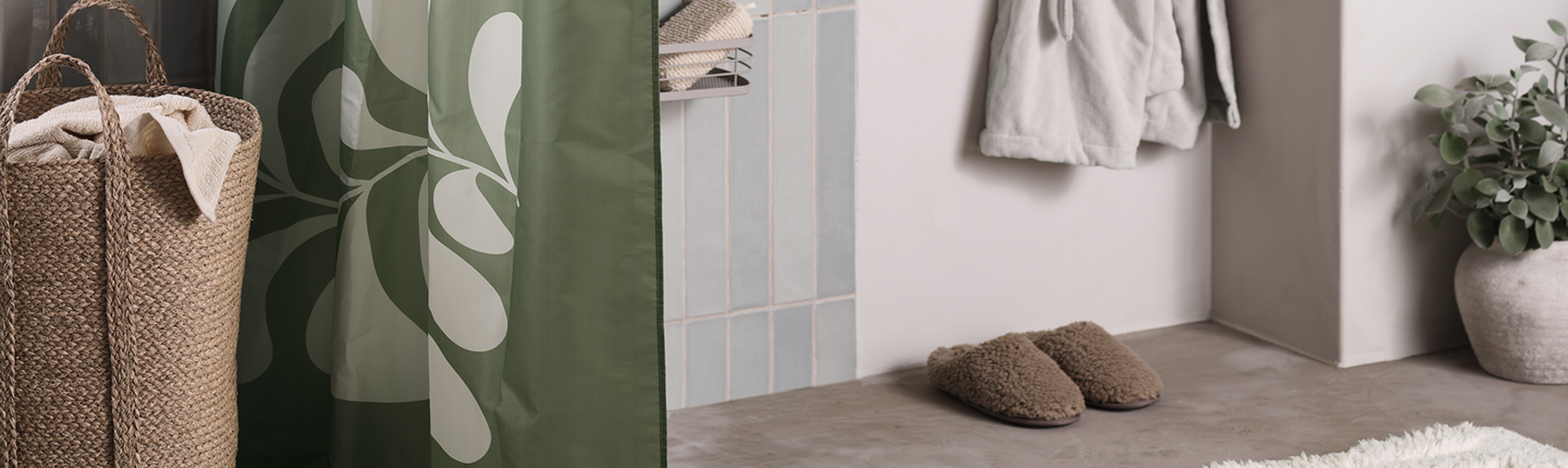 Bathroom cover Bathroom nook with a green leaf-patterned shower curtain beside a woven jute hamper, cozy slippers, and a hanging robe.