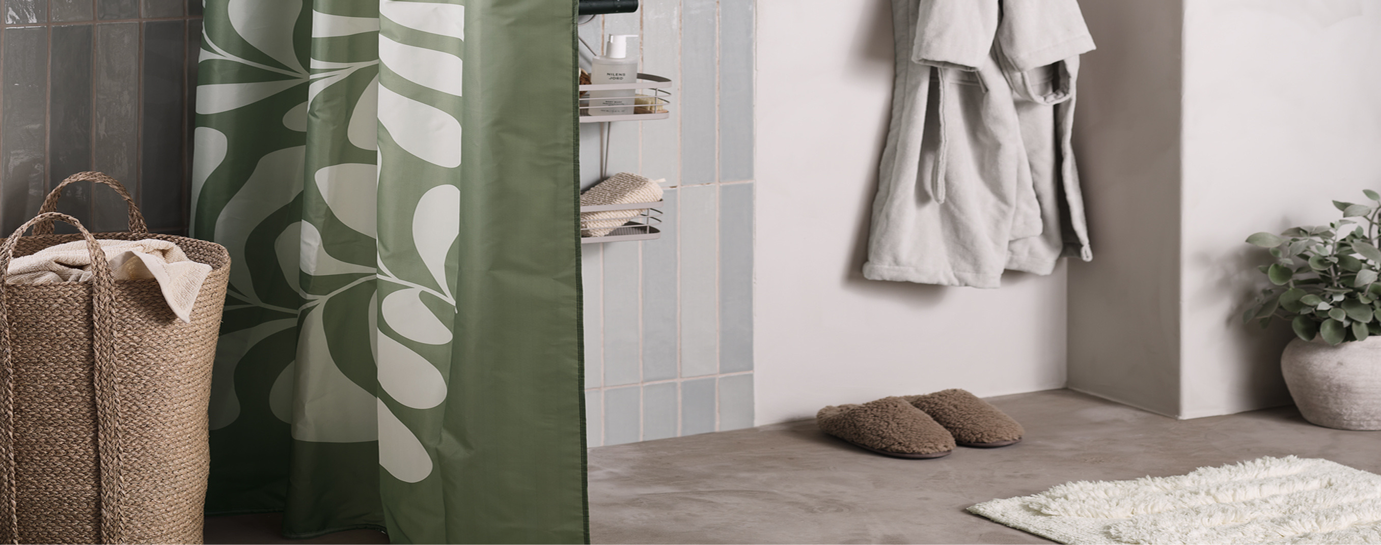 Bathroom cover Bathroom nook with a green leaf-patterned shower curtain beside a woven jute hamper, cozy slippers, and a hanging robe.