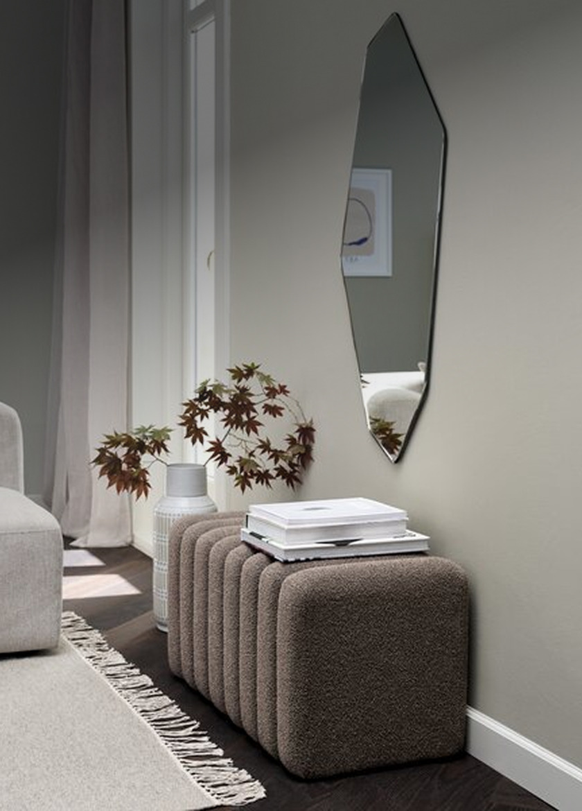 Benches Ribbed brown bouclé bench beneath an angular wall mirror in a hallway, styled with a ceramic vase of dried leaves and stacked books.