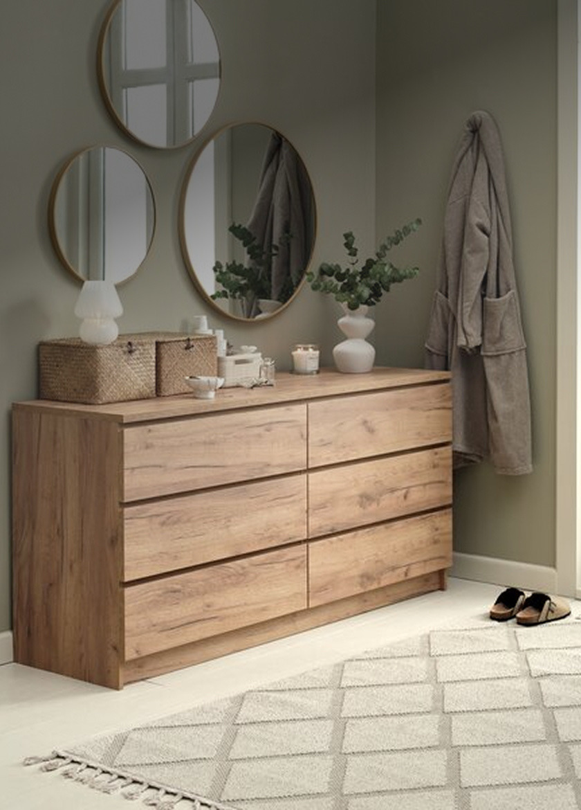 Chest of drawers Wood-finish six-drawer chest of drawers below three round mirrors, styled with woven baskets, candles, and a vase of eucalyptus.
