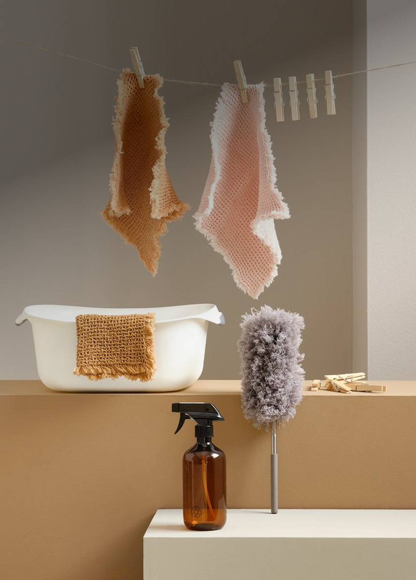 Cleaning products Pink and tan waffle-knit cloths hanging from clothespins above a wash basin, spray bottle, and duster.