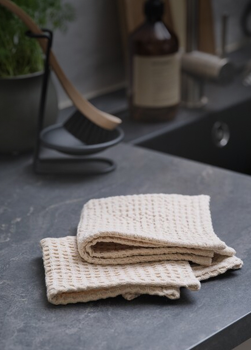 Cloths and sponges Folded beige waffle-knit cloths on a dark countertop, beside a cleaning brush stand and a bottle.