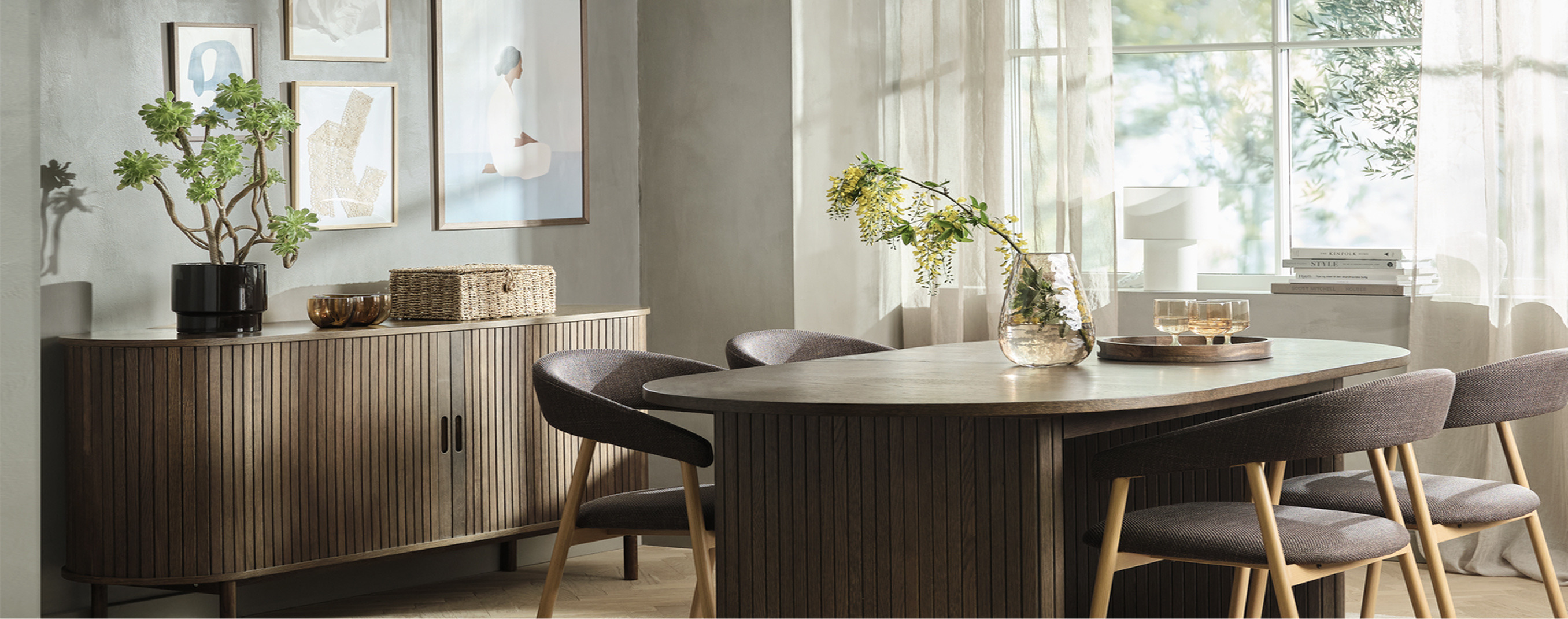 Dining room cover Dining room with a ribbed wood sideboard, framed art, and an oval wood table surrounded by upholstered chairs, with a glass vase of flowering branches.
