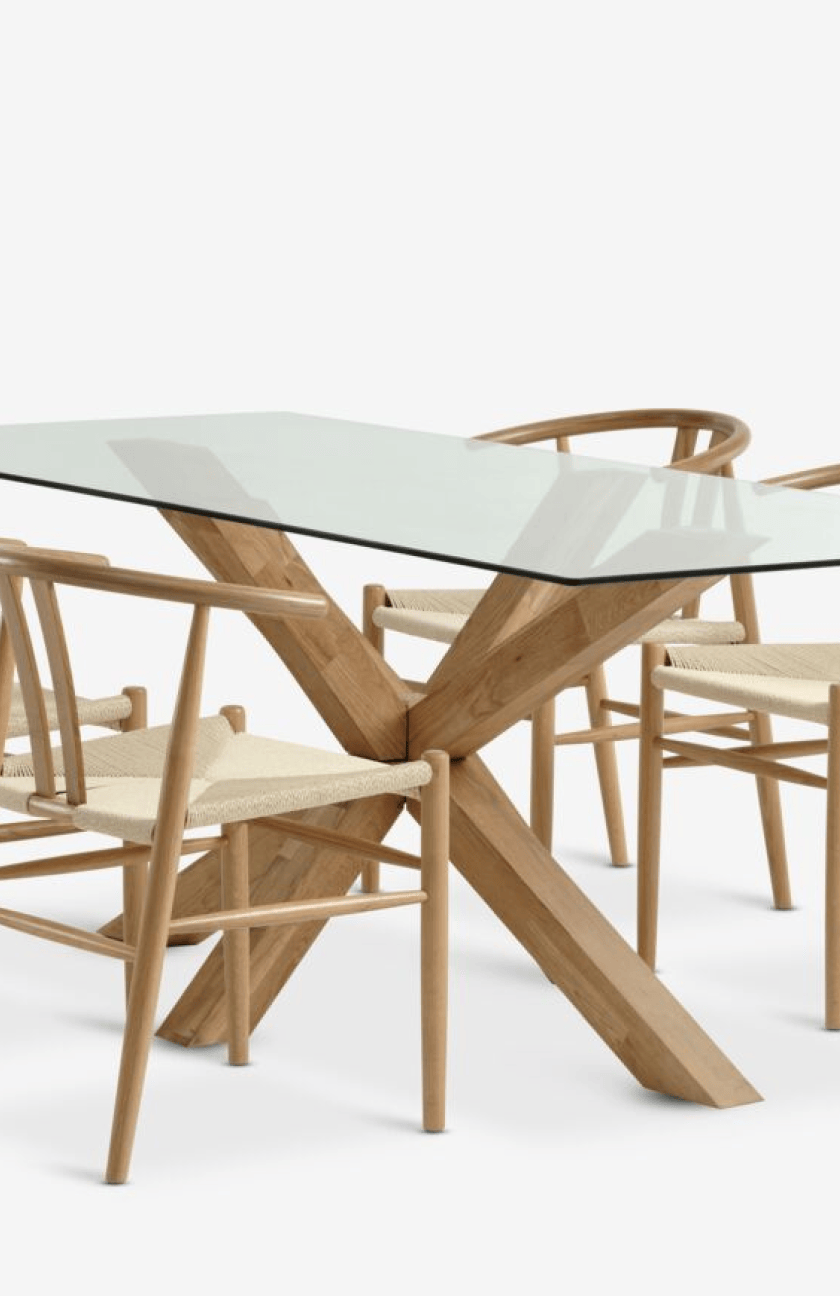 Dining sets Close-up of a glass-top dining table with a crossed oak leg base surrounded by wishbone-style dining chairs with woven seats.