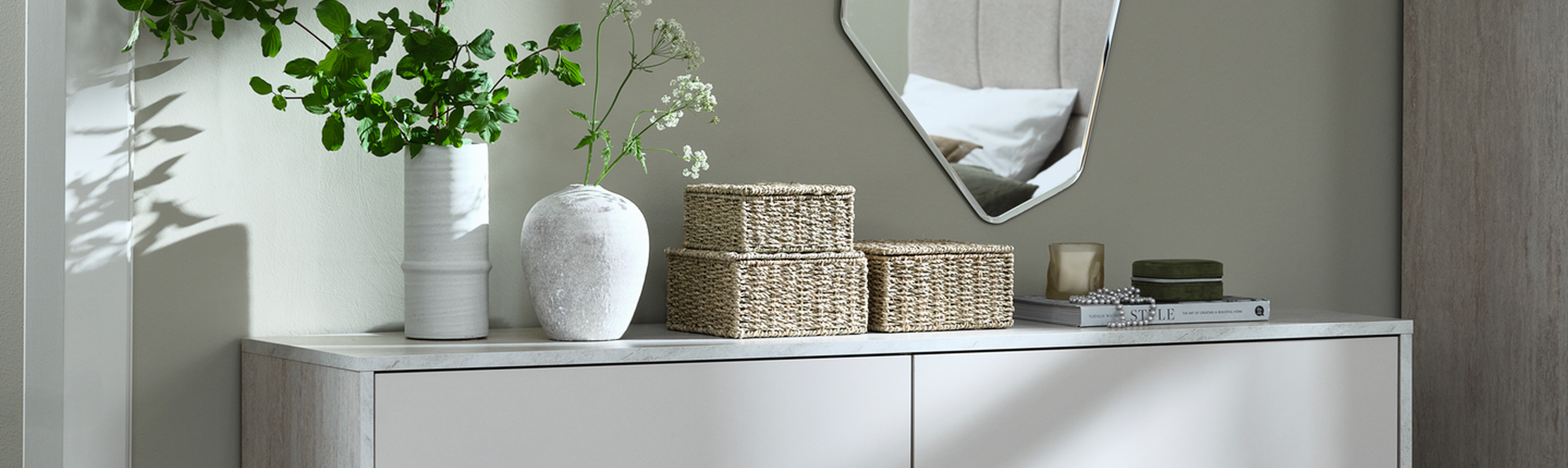 Hallway cover Hallway console table with woven storage baskets, ceramic vases with greenery, and an angular mirror reflecting a bedroom.