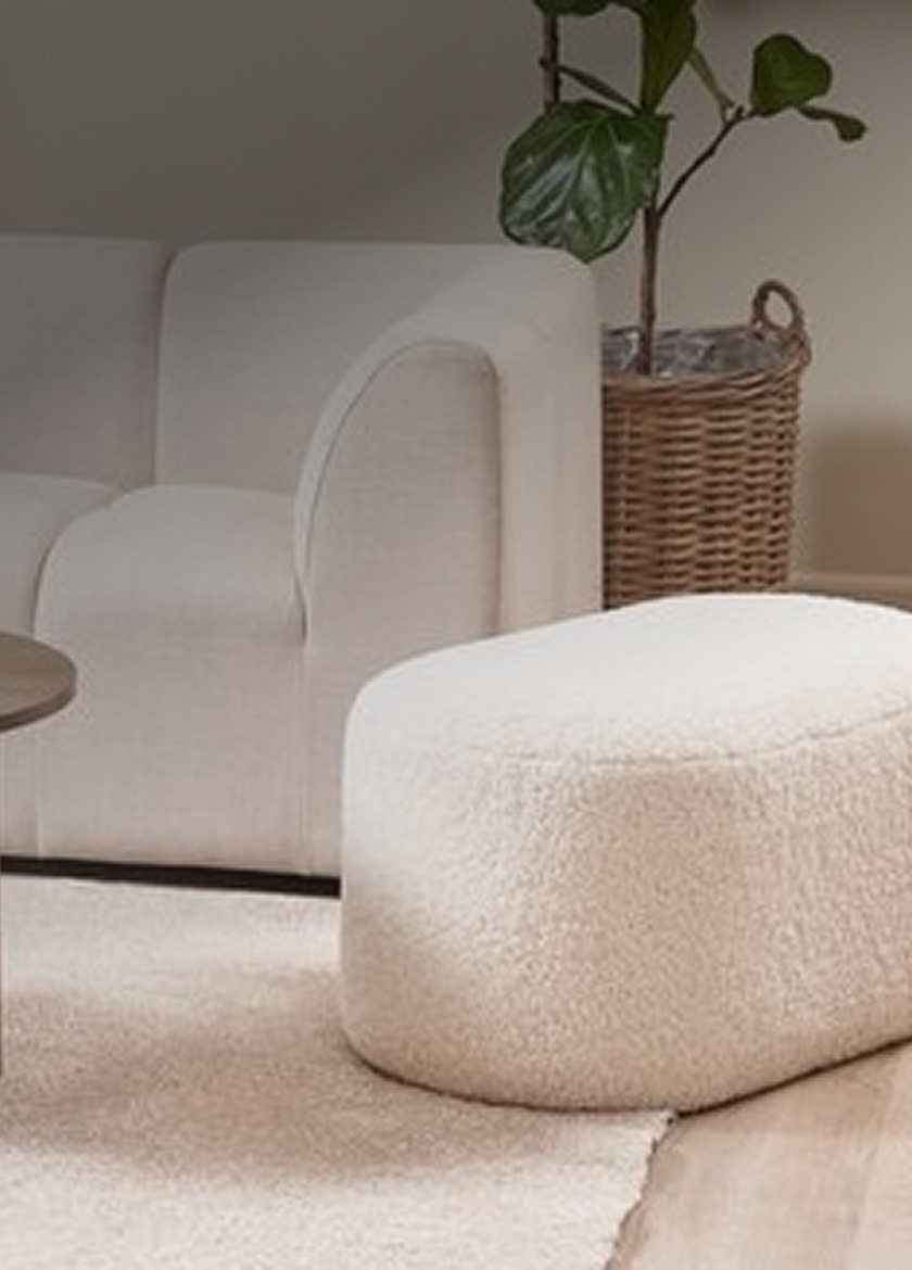 Pouffes Cream bouclé oval pouffe beside a woven rattan planter and a white sofa in a living room.