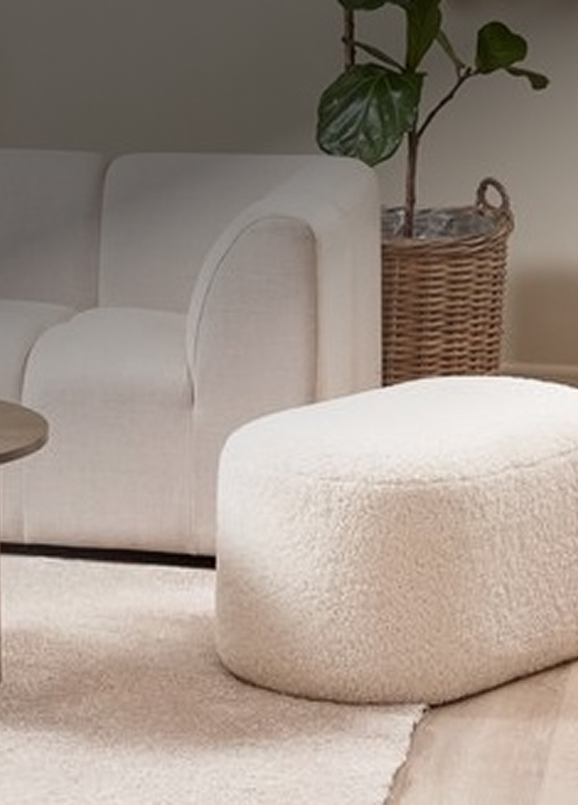 Pouffes Cream bouclé oval pouffe beside a woven rattan planter and a white sofa in a living room.