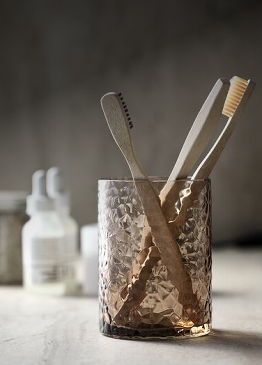 Toothbrush holders Textured glass tumbler holding two wooden toothbrushes, with toiletry bottles blurred in the background.