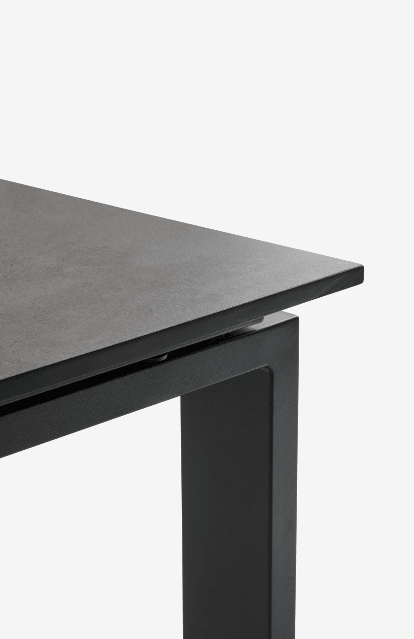 Composite tables Close-up corner of a black composite-top table with a black metal frame, shown against a plain white background.