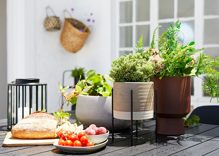 Keramikpflanzentopf, Laterne und Tablett mit Brot und Früchten auf dem Gartentisch