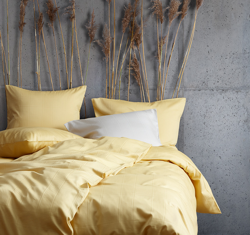 Gelbe Bettwäsche aus 51% recyceltem Polyester und 49% Baumwollsatin in einem Schlafzimmer mit Betonwänden