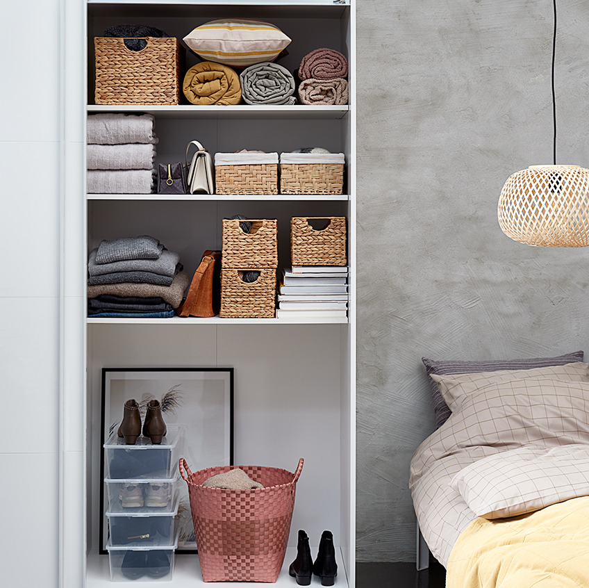 Schlafzimmer mit einem aufgeräumt wirkenden offenen Kleiderschrank mit Körben, Handtuch- und Taschenstapeln