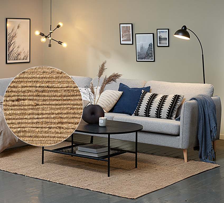 Wohnzimmer mit grauem Sofa und großem Juteteppich unter einem Couchtisch 