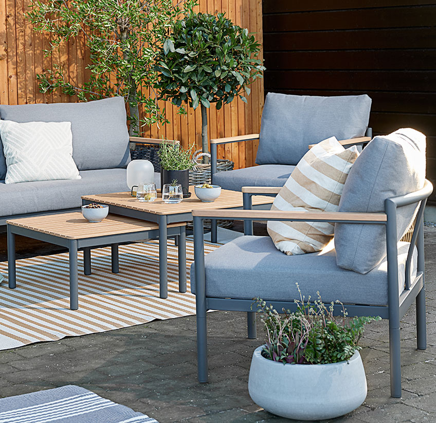 Garten-Lounge-Set mit bequemen Kissen auf einer Terrasse mit Teppichen und Pflanzgefäßen