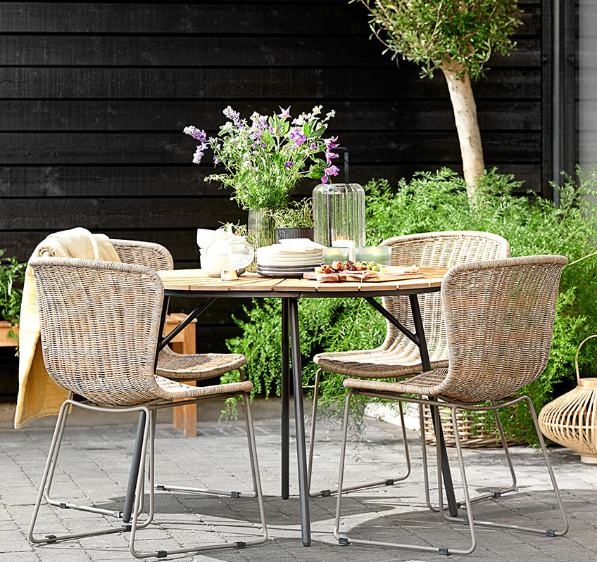 Vier Stapelstühle um einen runden Gartentisch auf einer Terrasse