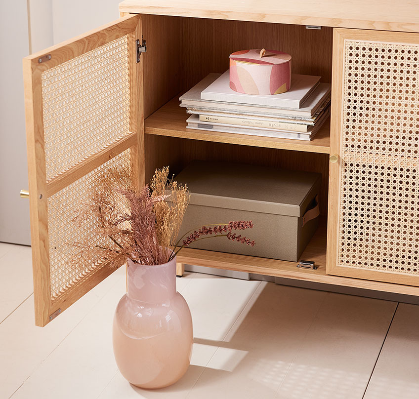 KASPER Vase und runde OLA Aufbewahrungsbox in HALMSTAD Sideboard Mundgeblasene Vase mit einem Strauß Kunstblumen vor einem Sideboard mit offener Tür und einer runden Aufbewahrungsbox darin