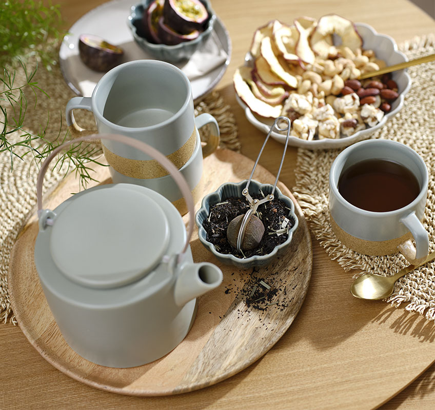 Dekotablett aus Holz, darauf eine grüne Teekanne, Tassen und Schüsseln mit Snacks und Tee