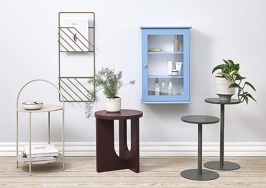 Beistelltisch ARCH, Blumenständer STAND IN, Wandschrank MALLING, Beistelltisch HALBY und Zeitschriftenhalter MAGSTRUP. Beistelltische, Blumenständer, Hängeschrank und goldener Zeitschriftenhalter nebeneinander präsentiert.