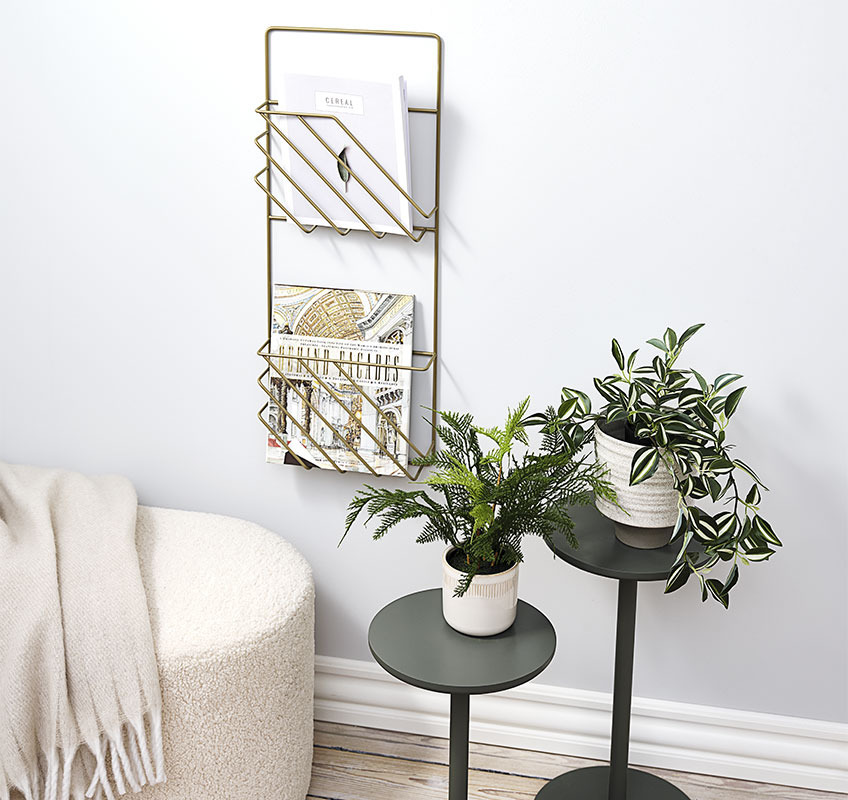 Der Blumenständer STAND IN und der Zeitschriftenhalter MAGSTRUP in Gold Zwei Blumenständer in olivgrün und ein goldener Zeitschriftenhalter, der an der Wand hängt.