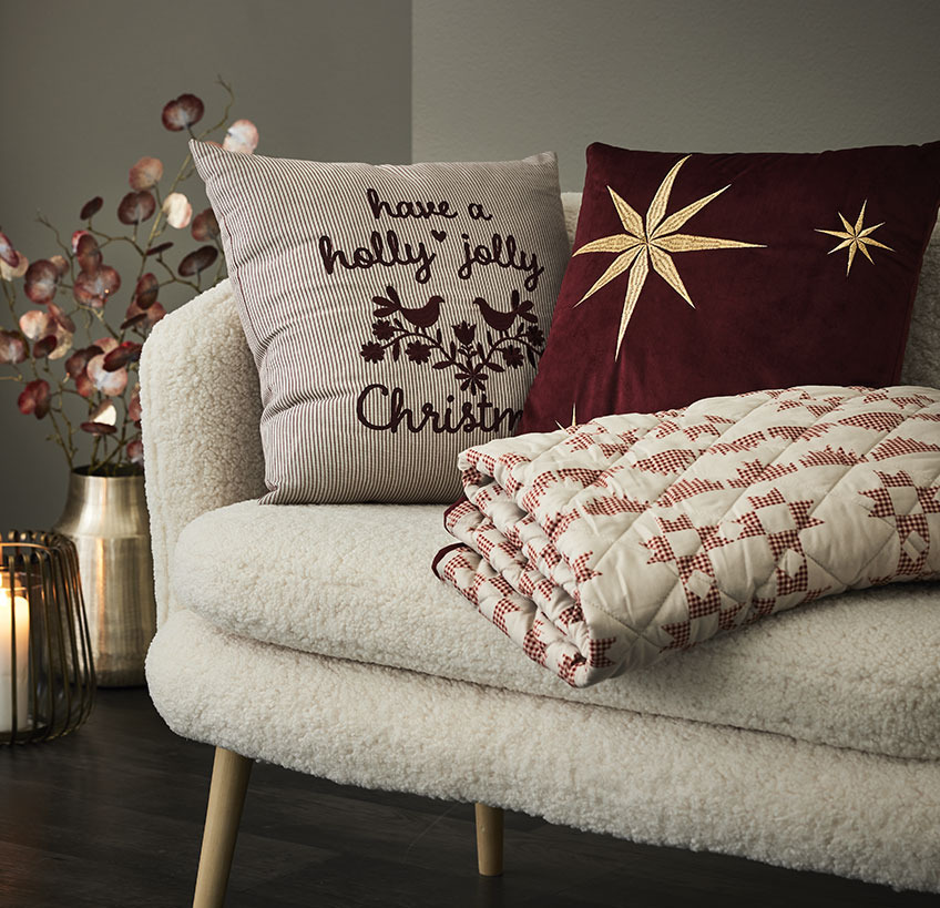 Kissen NIDHUG und RIND, Steppdecke TRILOBIT auf dem Sofa GISTRUP Kissen und Steppdecke mit Weihnachtsmotiven auf einem weißen Sofa
