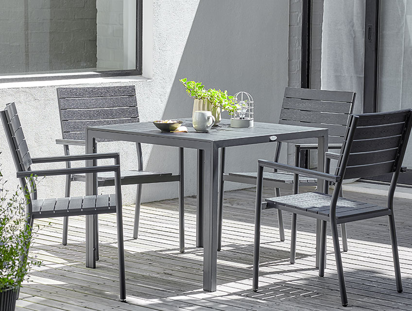 Quadratischer Gartentisch und vier Stapelstühle auf einer sonnigen Terrasse